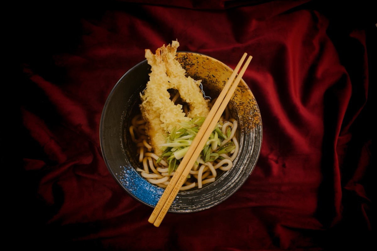 Tempura prawn udon in a ceramic bowl on deep red velvet, photographed from above